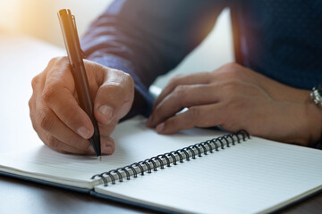 Close-up of man hand using writing pen memo on notebook paper or letter, diary on table desk office. Workplace for student, writer with copy space. business working and learning education concept.