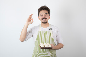 Portrait of smiling male cook holding raw mushrooms on white background