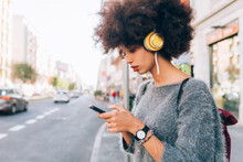 Young Woman Looking At Phone Outdoors, Wearing Headphones