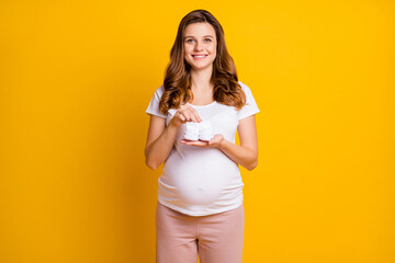 Sticker - Portrait of attractive careful cheerful pregnant girl holding in hands knitted socks unborn isolated over bright yellow color background