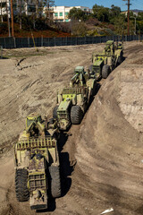 Wall Mural - Earthmoving vehicles following each other while scrapping dirt  as part of a grading project on a construction site