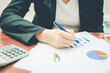 © thithawat - top view business woman working on table using pen point on business paper with financial accounting with growth statistics chart and graph for business analysis with calculator and tablet.