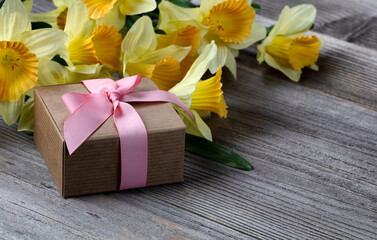 Close up view of a gift box with yellow daffodil on weathered wooden planks for Mothers day love holiday