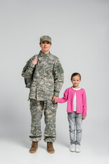 Wall Mural - Soldier with backpack holding hand of daughter on grey background