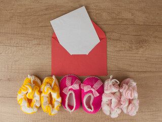 colorful handmade knitting baby shoes and envelope with blank paper sheet on wood table top.