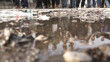 A Fast Motion Clip Of A Refugee Camp, Where Hundreds Of Them Are Standing In The Line For Food, The Refugees Are Reflected On A Dirty Water Puddle In Such A Way, That They Aren't Recognized. Serbia.