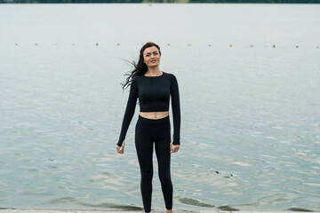 Active sporty fitness girl stretching legs during outdoor pier exercise, warm-up go evening jogging, sitting mat back to sunset near sea, motivated get perfect body, practicing yoga on fresh air.