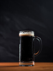 Wall Mural - Beer mug of fresh stout on a wooden table, dark background copy space