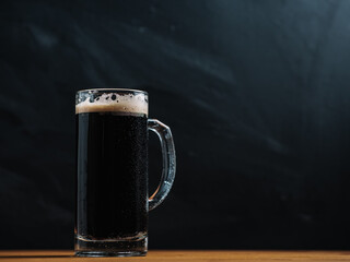 Beer mug of fresh stout on a wooden table, dark background copy space