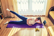 © Aliaksandr - Young beautiful woman in sportswear doing fitness workout at home, side-lying hip abduction, lateral leg raises, lie on left side on floor mat and lift right leg up, tablet and dumbbells on floor