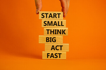 Wall Mural - Start small think big symbol. Words 'Start small think big act fast' on wooden blocks on a beautiful orange background. Businessman hand. Business, motivational and start small think big concept.