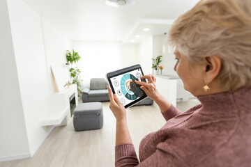technology, automation and efficiency concept - smiling senior woman in glasses with tablet computer using smart home app over grey background
