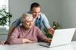 © Angelov - Adult mother and son consider new software on laptop sitting at table