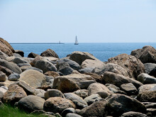 Rocky Shoreline With Sailboat In The Background. Coast Of Hammonasset Beach State Park In Madison. Connecticut.