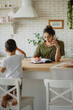 © Olena Bloshchynska - Back view of a boy playing at kitchen while his mother making a notes and speaking on a phone.