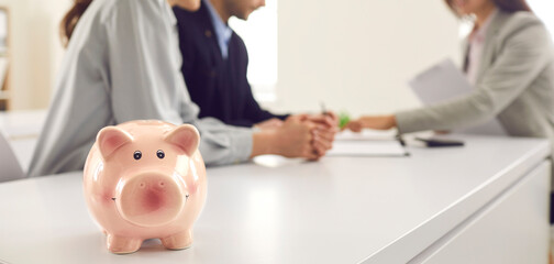 Couple consulting bank agent or manager. Young people investing money, opening account, asking for financial advice or getting loan to buy new car, house or apartment. Copyspace banner with piggy bank