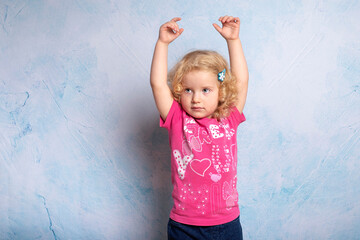 Portrait of a cute little curly blonde 2 year old girl of 
 blue background