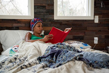 African American woman reading book in bed