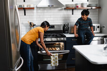 Indian Mother And Son Putting Cookie Dough In Oven To Bake