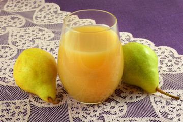 Pear juice in a drinking glass with fresh raw bartlett pears on pink lace table runner on purple tablecloth