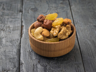 A wooden bowl with a mixture of nuts and dried fruits on a black wooden table.