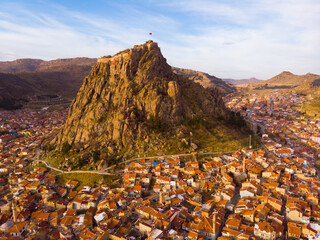 Wall Mural - View from drone of residential districts of Turkish city of Afyonkarahisar overlooking volcanic rock with ancient ruined castle on top on winter day, Afyon Province