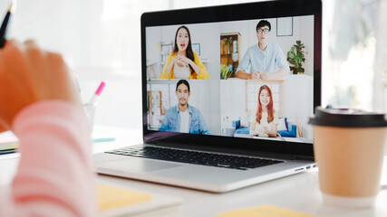 Wall Mural - Young Asia businesswoman using laptop talk to colleague about plan in video call meeting while work from home at living room. Self-isolation, social distancing, quarantine for corona virus prevention.