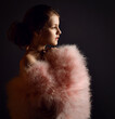 Portrait of gentle little kid girl, teen countess lady in furry clothes with big sleeves and bared shoulders looking hopefully into the distance over dark background. Side view