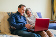 © miguel - Cheerful adult couple sitting on a couch and watching a program on a laptop. selective focus.