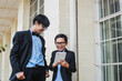 © Gatot - Two brothers wearing glasses, black ribbon and black suit jacket joking with smart phone or tablet