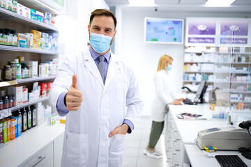 Wall Mural - Portrait of handsome caucasian male pharmacist with face mask standing in pharmacy store.