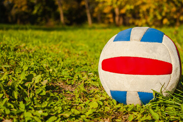 An old multi-colored volleyball ball is lying on the green grass, close-up. Free space for the text