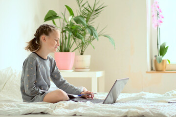 Wall Mural - Additional activities at home. Smiling beautiful girl doing homework while sitting on the bed at home. Close-up. Side view.