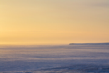 Wall Mural - winter arctic landscape. morning aerial view of snowy tundra and frozen sea. in the distance is a ca