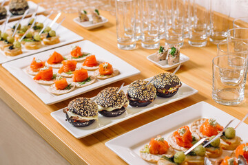 Wall Mural - A plate of mini burgers, black buns sprinkled with white sesame seeds. There are salmon roll dishes nearby