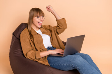 Poster - Photo of blond hooray lady sit on bag talk laptop wear spectacles shirt jeans sneakers isolated on beige color background