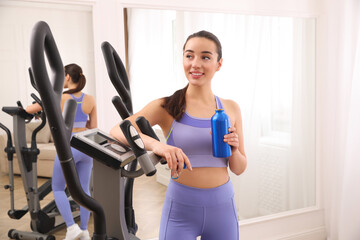 Canvas Print - Woman with bottle near elliptical machine indoors