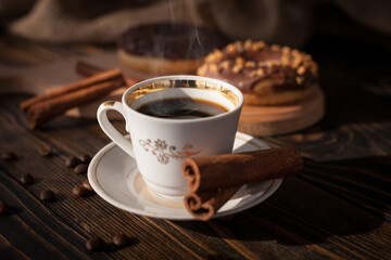 A cup of aromatic black coffee and coffee beans on the table. Morning espresso coffee for breakfast in a beautiful white cup. With a delicious donut in the background. 