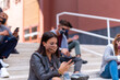 © MandriaPix - sad young woman looking at the smartphone, addiction to social media, chat and message on line, group of multiracial student at college wearing face mask