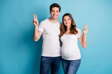 Poster - Photo of cheerful positive beautiful good mood family waiting baby showing v-sign isolated blue color background