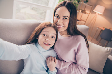 Wall Mural - Photo of optimistic brunette red hairdo mom daughter hold hands do selfie sit on sofa wear sweater pants at home