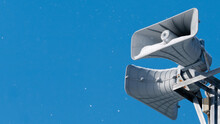 Close-up. Two Square Loudspeakers Covered With Snow Against A Blue Sky With Snowflakes. Population Warning System. Free Space For Text.