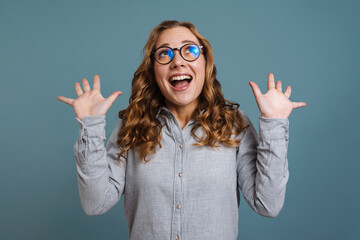 Excited girl in eyeglasses smiling while posing with hands up