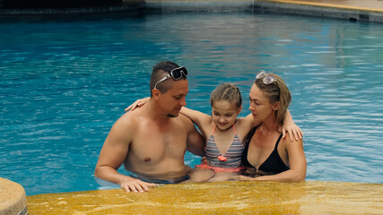 The mother and father with little daughter have fun in the pool. Mom and dad plays with the child. The family enjoy summer vacation in a swimming pool jumping, spinning, splash water. Slow motion.