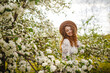 © Konstantin Zibert - Portrait of a young girl with curly hair standing in the middle of a blooming tree surrounded by lots of white flowers. Female wearing beige hat and white dress on a bright spring day.
