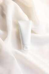 white cosmetic tube for face cream, cleanser, body lotion or shampoo on white draped cloth. Gentle skin care concept.