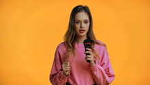 Teenage Girl In Pink Sweatshirt Talking While Holding Microphone Isolated On Yellow