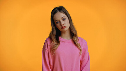 Wall Mural - sad teenage girl in pink sweatshirt looking at camera isolated on yellow