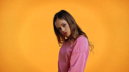 Wall Mural - teenage girl in pink sweatshirt looking at camera isolated on yellow