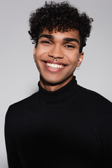 curly african american man in black turtleneck sweater smiling isolated on grey